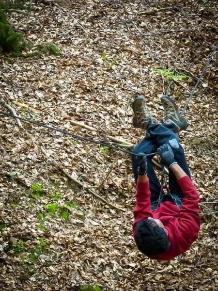 Überquert eine selbstgebaute Seilbrücke in einem Laubwald