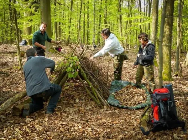 Vier Personen bauen eine Tarp-Notunterkunft aus Ästen im Wald