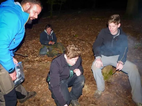 Zunder glimmt neben sitzenden Personen im Wald, Rauch steigt auf