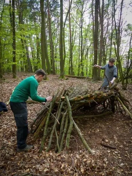 Zwei Personen bauen eine Holzstruktur als Notunterkunft im Wald