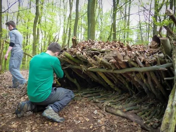 Zwei Personen bauen eine Laubhütte aus Ästen und Blättern im Wald