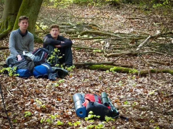 Zwei Personen sitzen auf dem Boden neben Rucksäcken im Wald