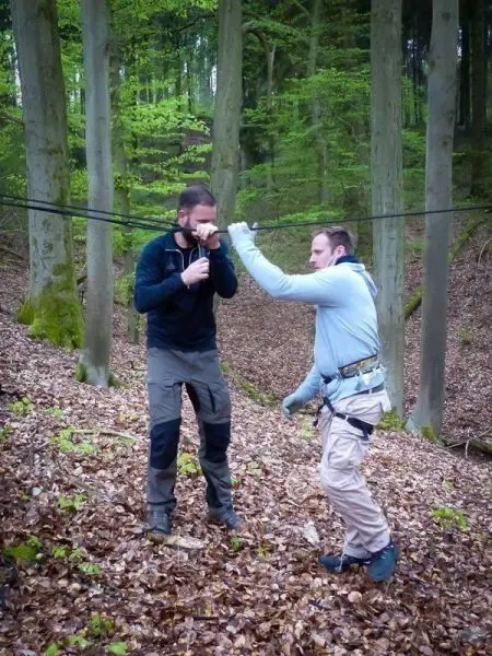 Zwei Personen überqueren eine selbstgebaute Seilbrücke zwischen Bäumen