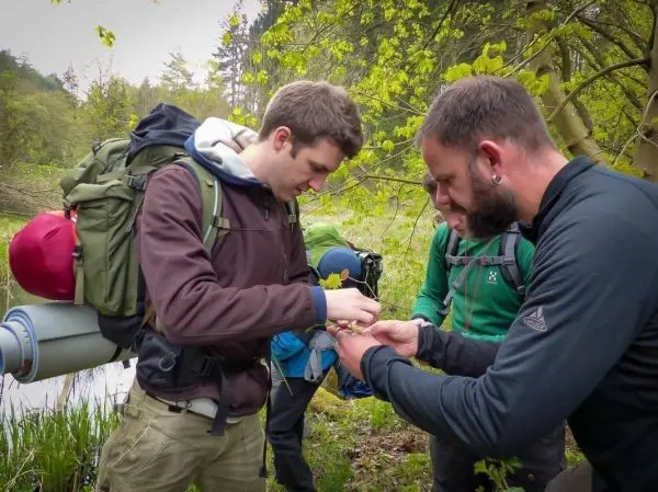 Zwei Personen untersuchen gemeinsam ein kleines Objekt am Ufer eines Gewässers