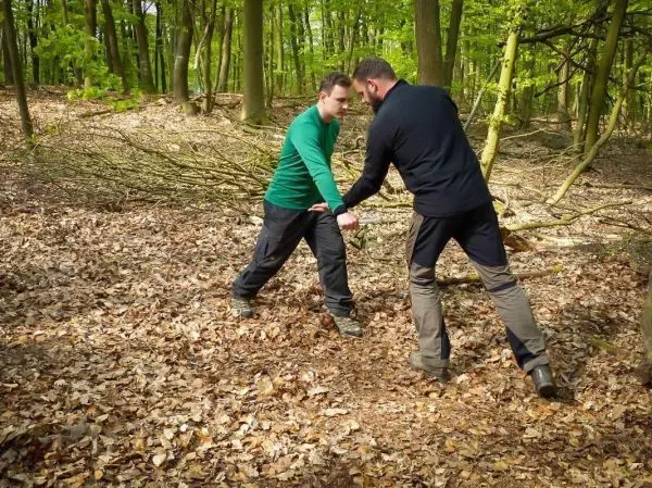 Zwei Personen ziehen an einem dicken Ast im Wald