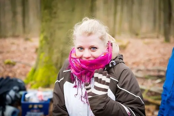 Eine Person mit rosa Schal und Handschuhen lächelt in einem Wald