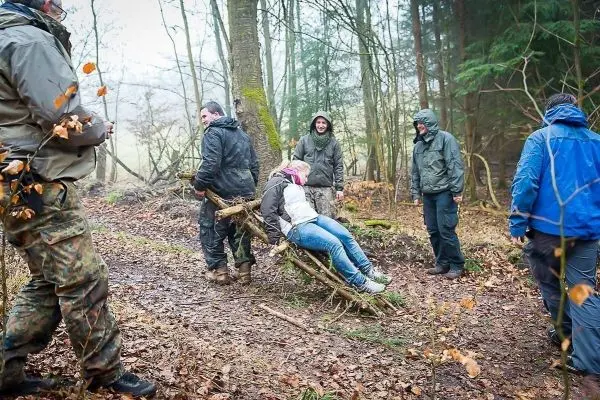 Gruppe transportiert verletzte Person auf improvisierter Trage durch den Wald