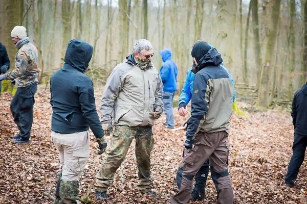Gruppe von Personen steht im Wald und diskutiert miteinander