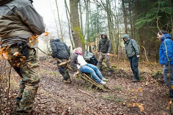 Gruppierung zieht improvisierte Trage mit verletzter Person durch den Wald