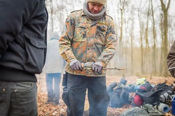 Mann bearbeitet Holzstück mit Messer in einem Waldgebiet