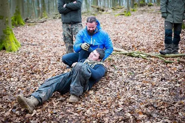 Mann liegt auf dem Boden, während ein anderer ihn mit einer improvisierten Trage bewegt