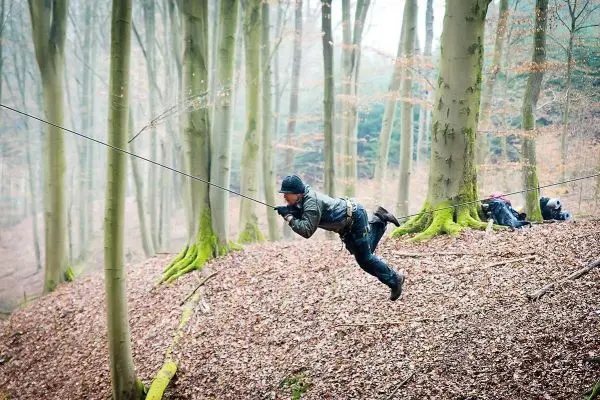 Mann überquert eine selbstgebaute Seilbrücke zwischen Bäumen im Wald