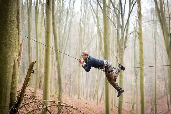 Mann überquert eine selbstgebaute Seilbrücke zwischen zwei Bäumen
