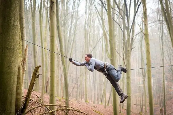 Mann überquert selbstgebaute Seilbrücke zwischen Bäumen im Wald