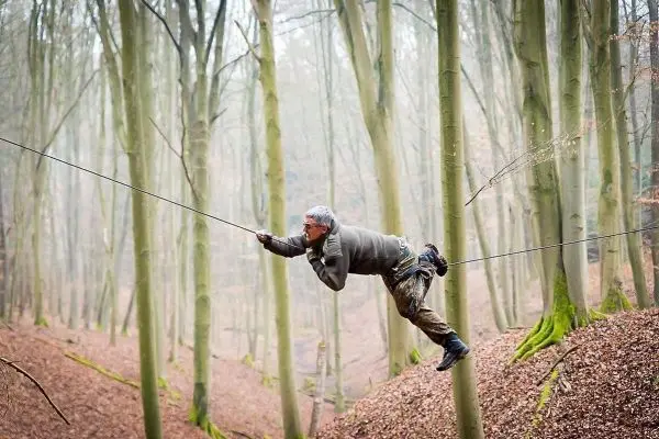 Mann überquert selbstgebaute Seilbrücke zwischen Bäumen im Wald