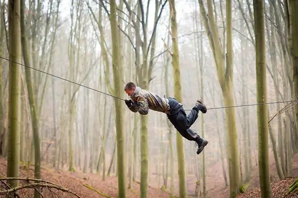 Mann überquert selbstgebaute Seilbrücke zwischen Bäumen im Wald
