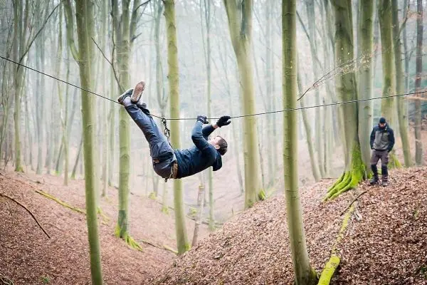 Mann überquert selbstgebaute Seilbrücke zwischen Bäumen im Wald