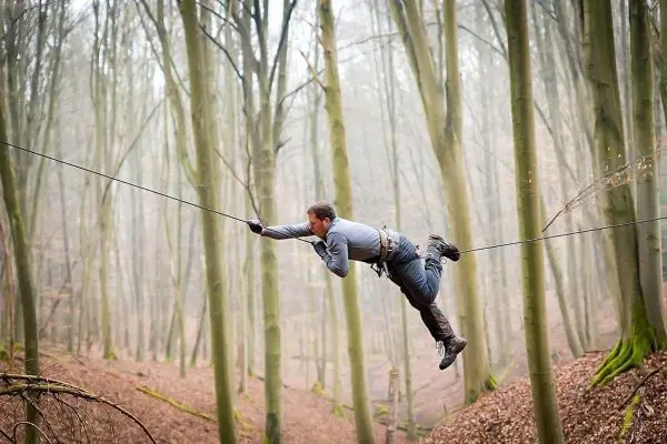 Mann überquert selbstgebaute Seilbrücke zwischen Bäumen im Wald