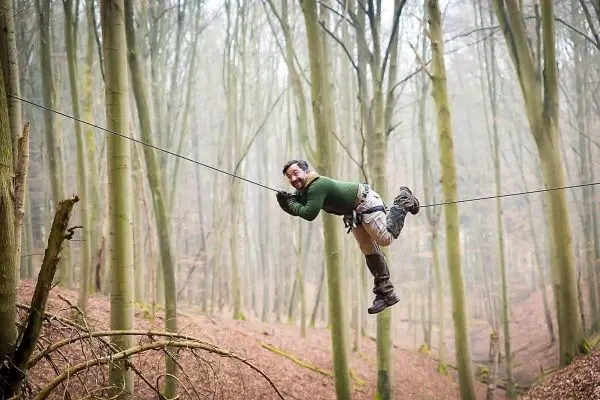 Mann überquert selbstgebaute Seilbrücke zwischen Bäumen im Wald