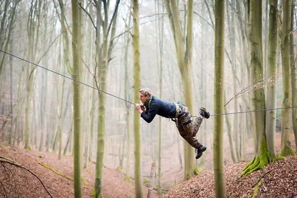 Mann überquert selbstgebaute Seilbrücke zwischen Bäumen im Wald