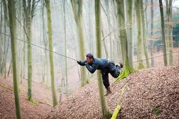 Mann überquert selbstgebaute Seilbrücke zwischen zwei Bäumen