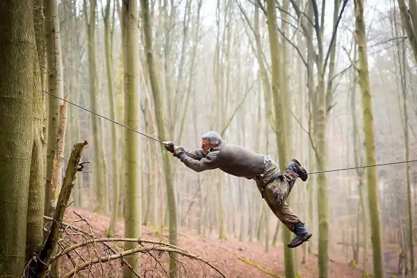 Mann überquert selbstgebaute Seilbrücke zwischen zwei Bäumen