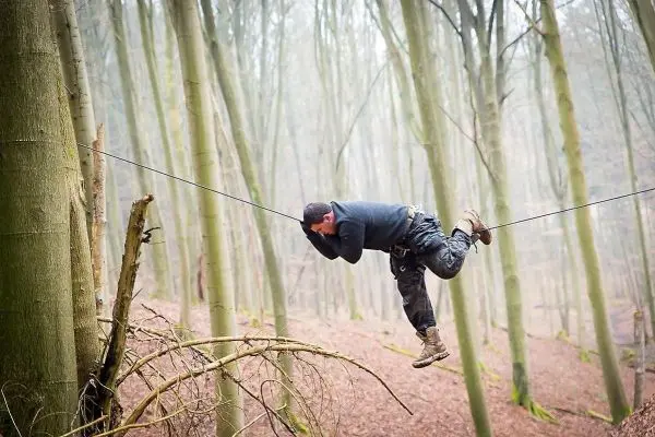 Mann überquert selbstgebaute Seilbrücke zwischen zwei Bäumen