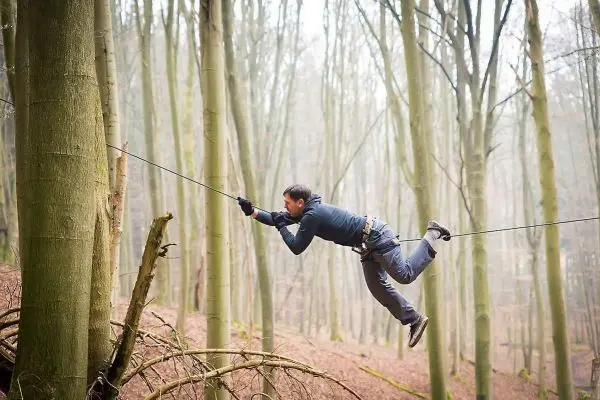 Mann überquert selbstgebaute Seilbrücke zwischen zwei Bäumen im Wald