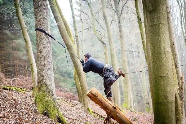 Mann überquert selbstgebaute Seilbrücke zwischen zwei Bäumen im Wald