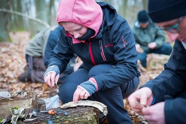 Person bearbeitet Holzstück mit einem Messer im Wald