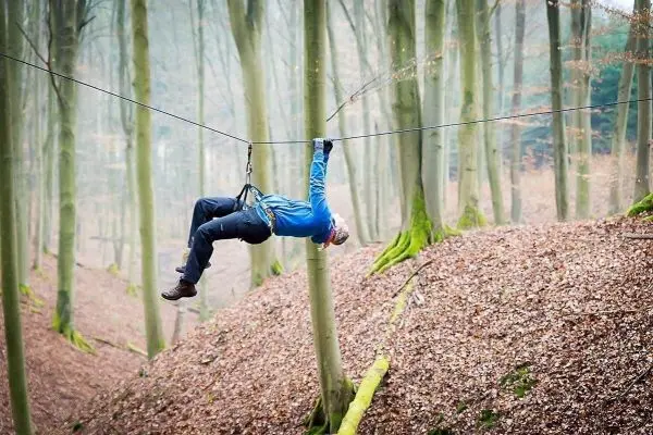 Person hängt an einer Seilbrücke zwischen Bäumen beim Überlebenstraining