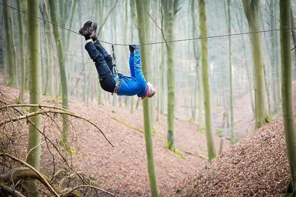 Person hängt kopfüber an einem Seil zwischen Bäumen