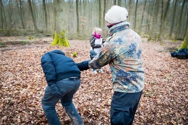 Person in camouflagierter Jacke hält andere Person am Arm im Wald