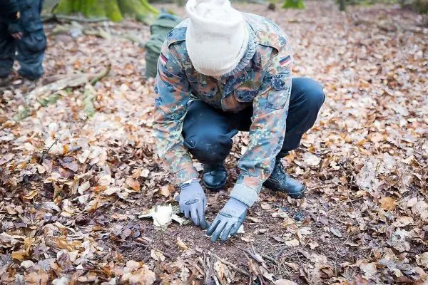 Person kniet im Laub und bereitet den Boden für eine Feuerstelle vor