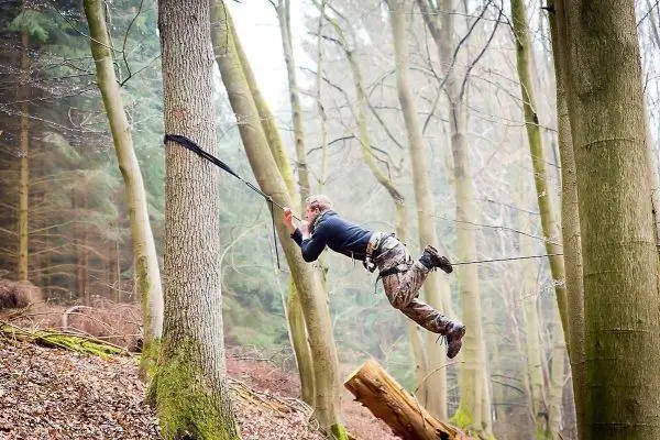 Person schwingt an Seil zwischen Bäumen im Wald