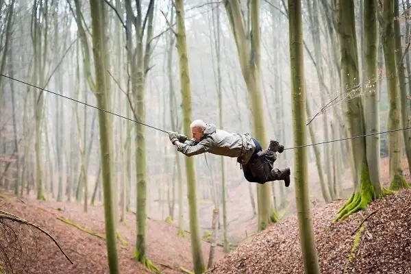 Person schwingt an selbstgebauter Seilbrücke durch den Wald