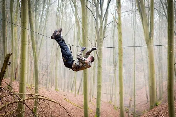 Person schwingt an selbstgebauter Seilbrücke durch den Wald