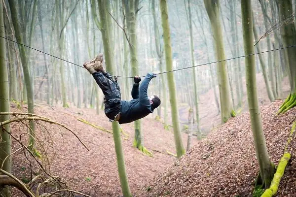Person schwingt an selbstgebauter Seilbrücke zwischen Bäumen