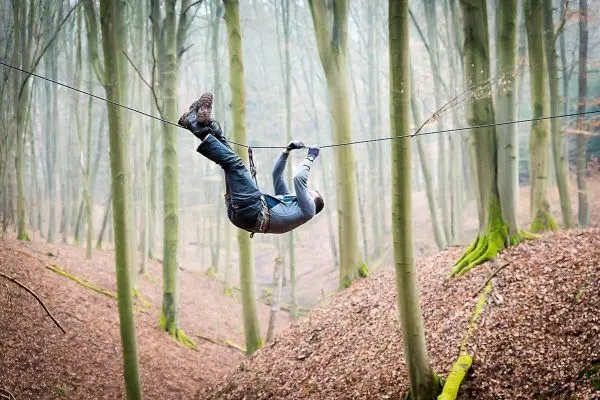 Person schwingt an selbstgebauter Seilbrücke zwischen Bäumen
