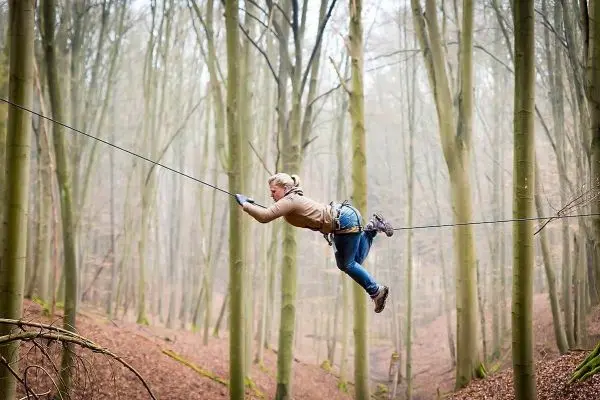 Person schwingt an selbstgebauter Seilbrücke zwischen Bäumen beim Survival Training