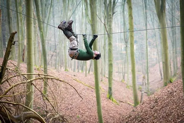 Seilquerung über einen Waldweg, Person hängt kopfüber an einem Seil