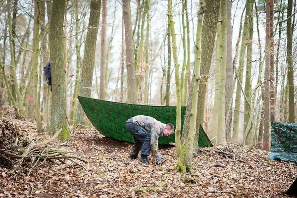 Tarp-Notunterkunft wird im Wald zwischen Bäumen aufgestellt