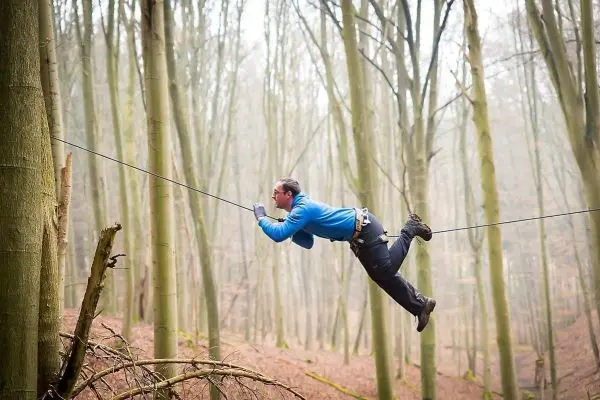 Überquert eine selbstgebaute Seilbrücke zwischen zwei Bäumen im Wald