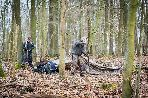 Zwei Personen bauen eine Tarp-Notunterkunft im Wald auf