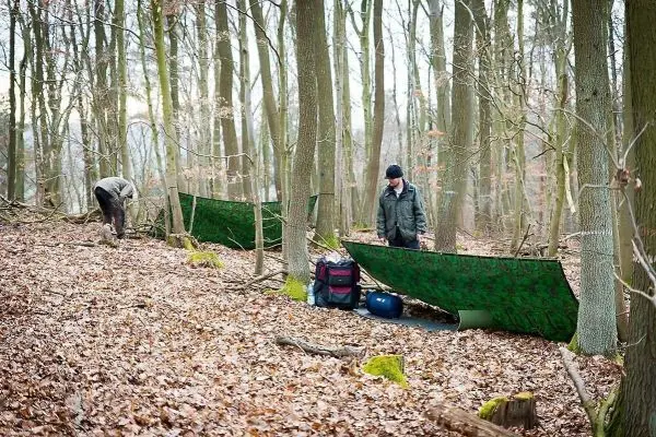 Zwei Personen bauen Tarp-Notunterkünfte im Wald auf