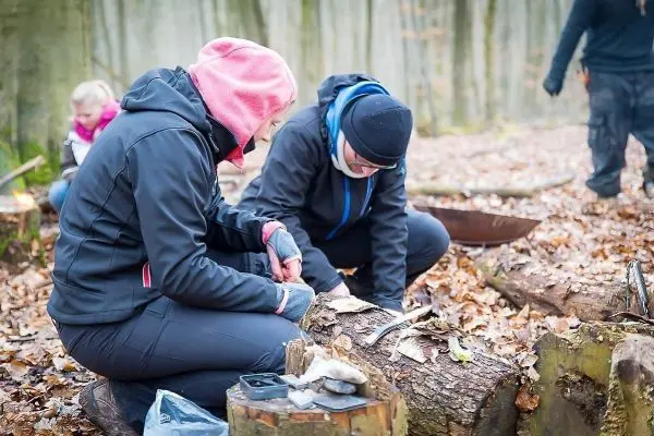 Zwei Personen bearbeiten Holzstücke auf dem Boden im Wald