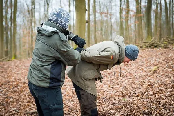 Zwei Personen in Waldumgebung, eine Person hält die Hände der anderen hinter dem Rücken