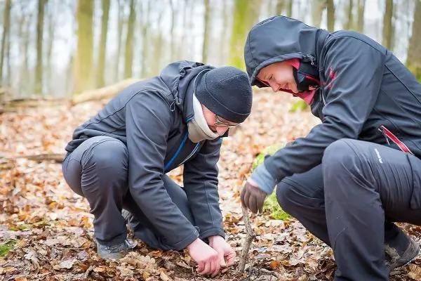 Zwei Personen knien im Laub und bearbeiten einen Stock im Wald