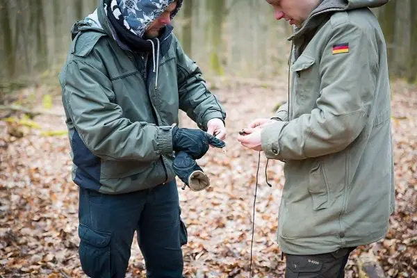 Zwei Personen knoten ein Seil im Wald auf Laubboden