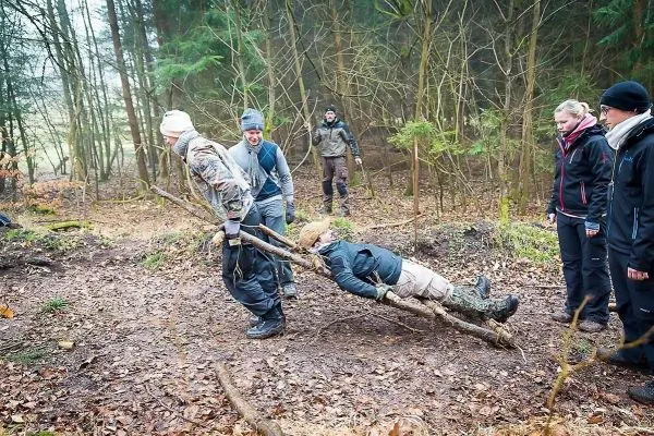 Zwei Personen tragen eine improvisierte Trage aus Ästen mit einer liegenden Person